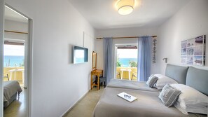 Une chambre avec deux lits, un bureau, une chaise et une vue sur la mer.