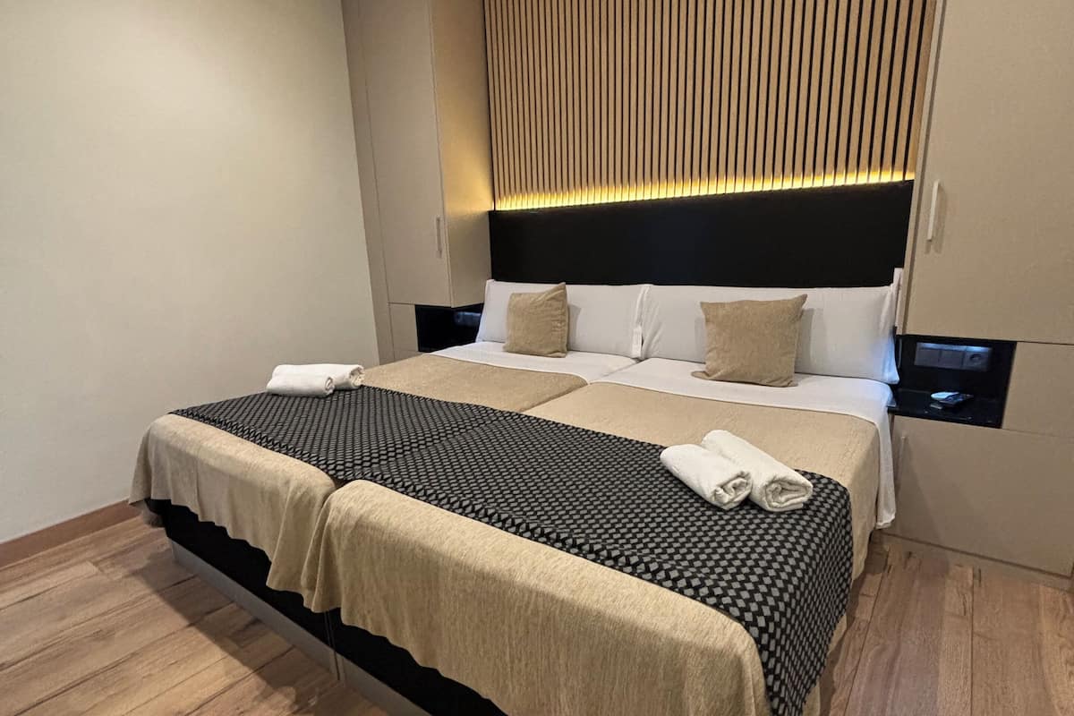 Quarto de hotel moderno com cama grande, piso de madeira e cabeceira fixada na parede com ripas verticais.