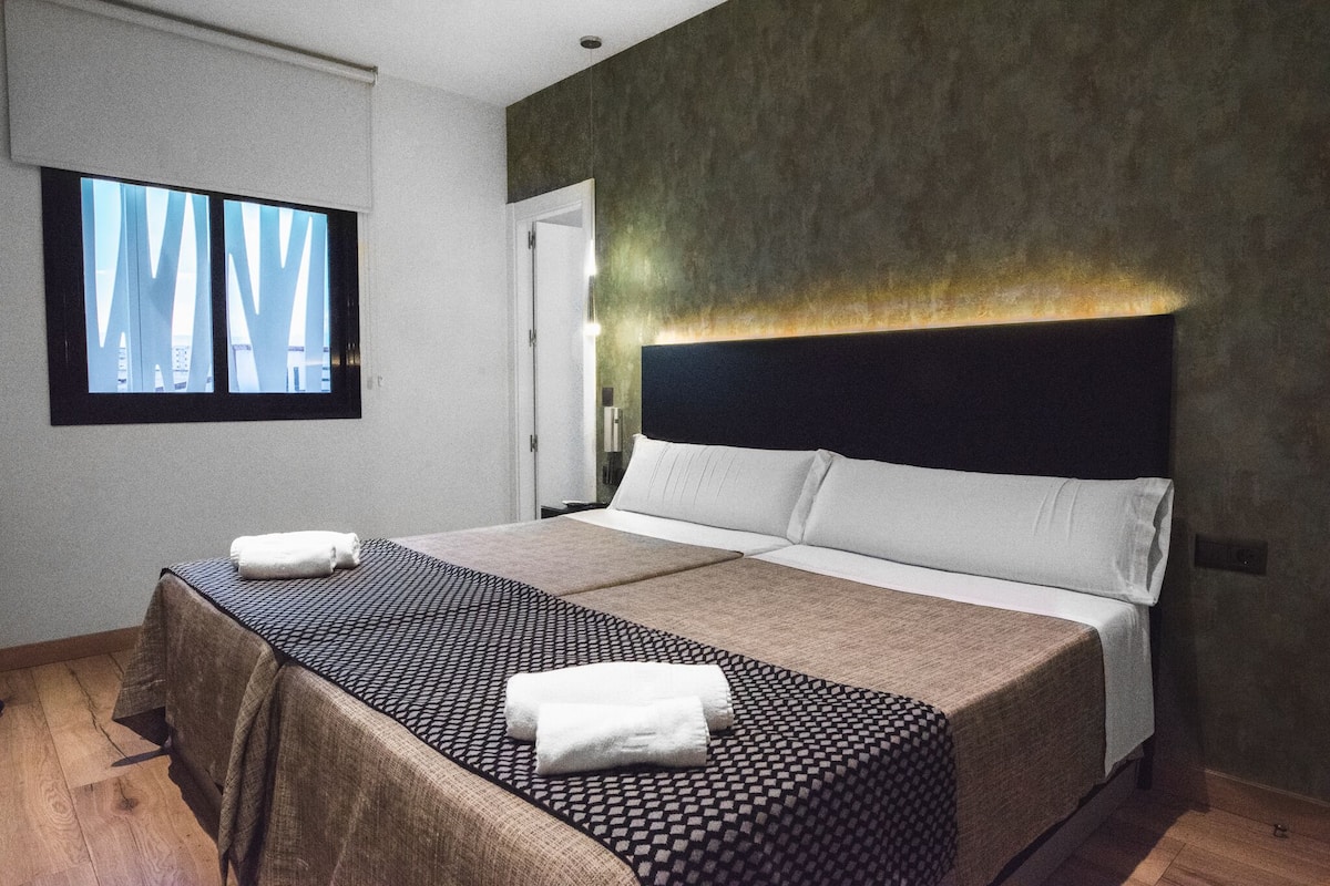 Quarto de hotel moderno com uma cama grande, vista para edifícios através de uma janela e parede com textura.