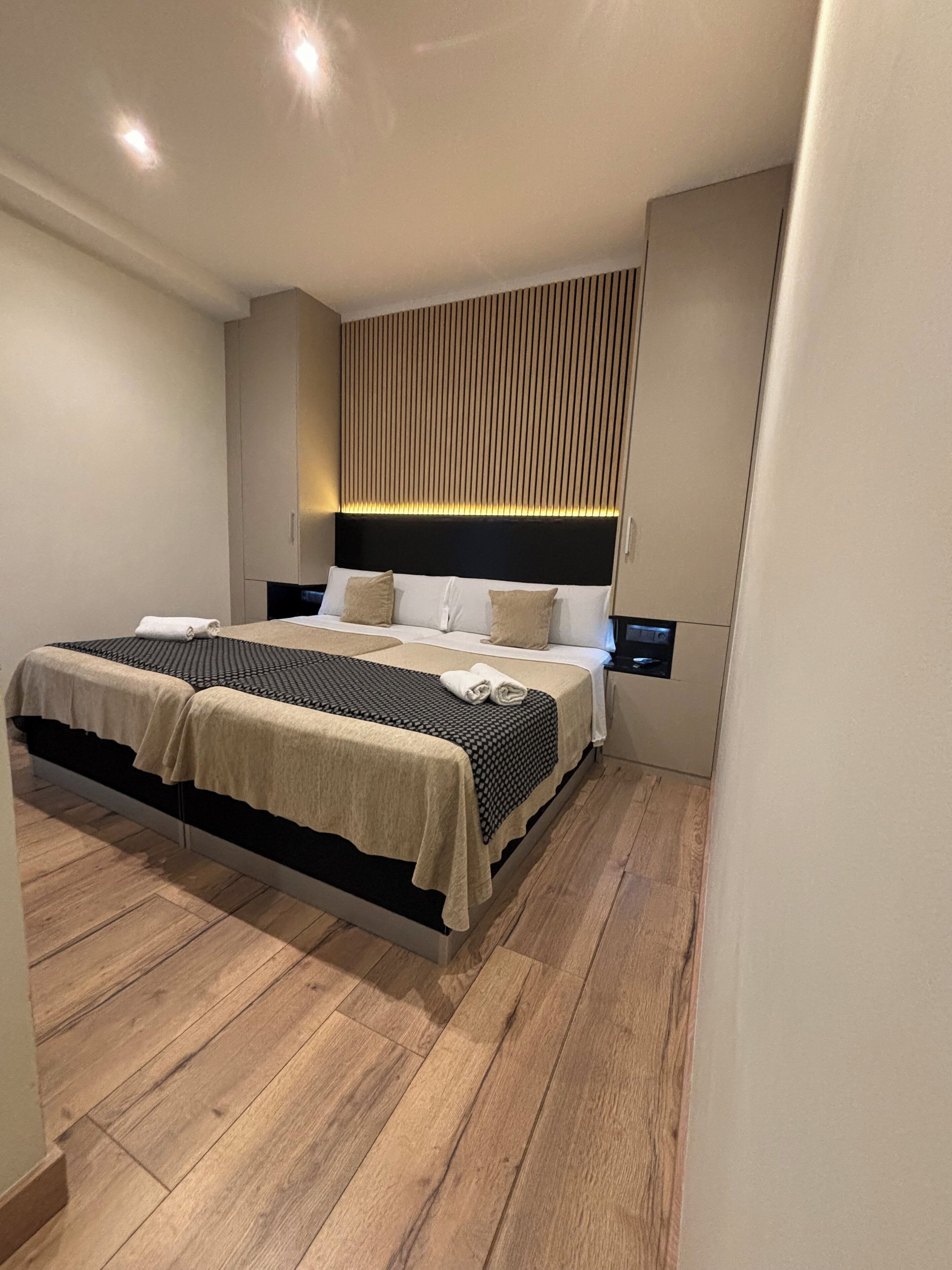 A modern bedroom with a bed, wooden flooring, and a wall-mounted light fixture.