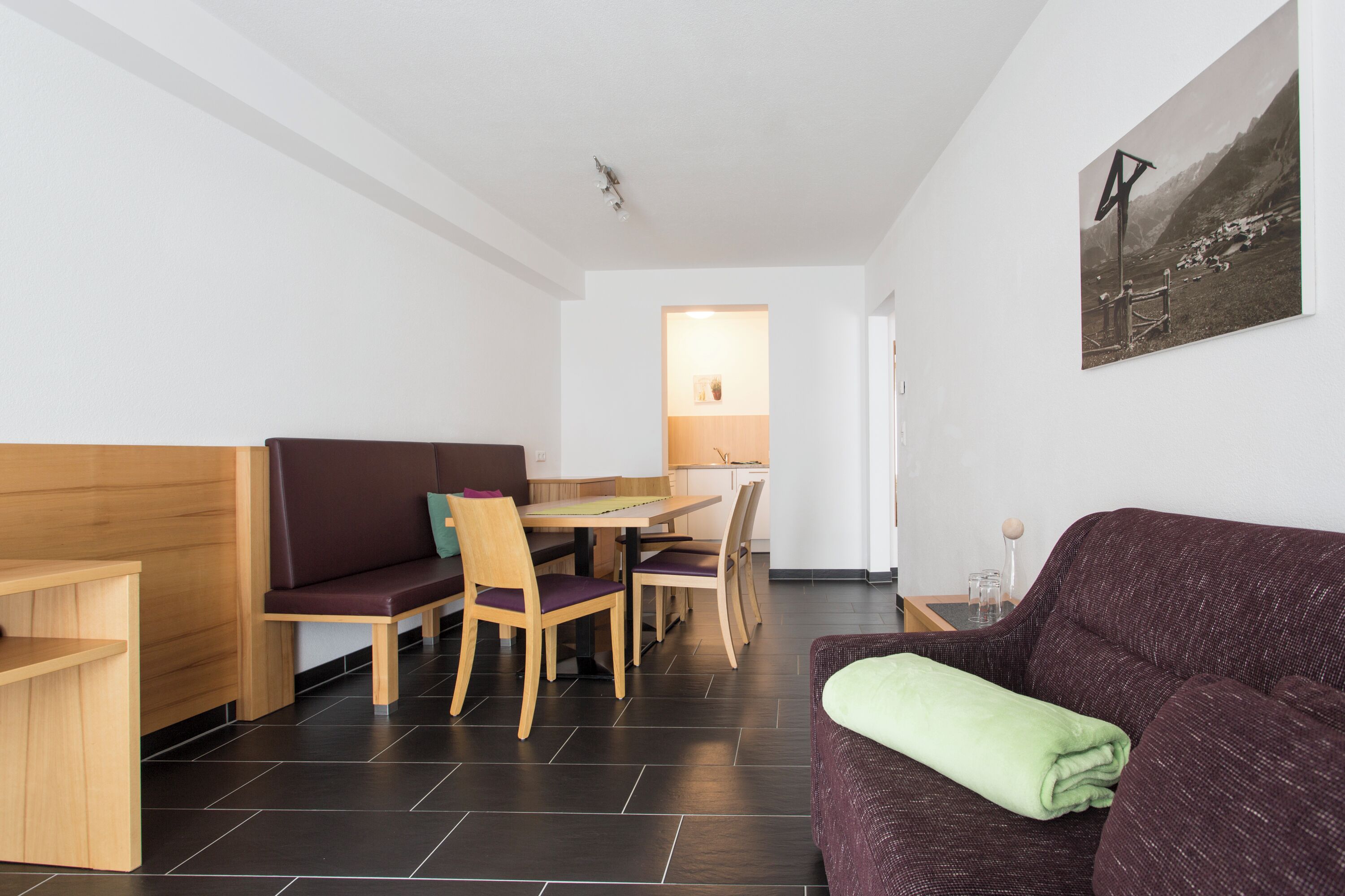 Een moderne kamer met een houten bank, een paarse bank, een eettafel met stoelen en een schilderij aan de muur.