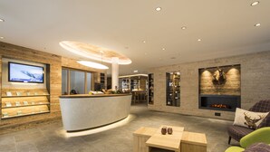 A modern lobby with a reception desk, seating area, fireplace, and a television displaying a snowy landscape. - Das Landerer (Ladis)