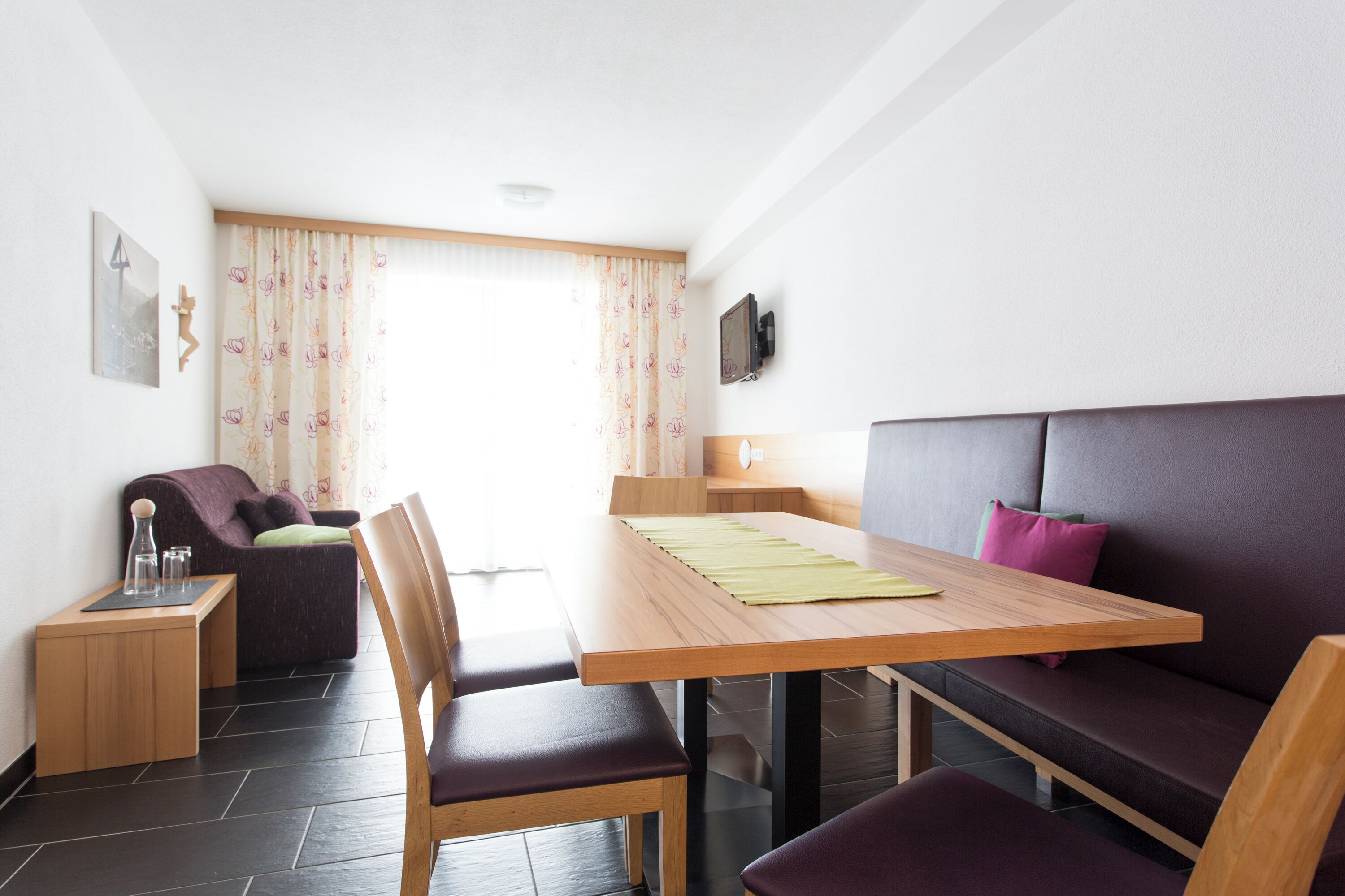 Una habitación moderna con una mesa de madera, un sofá púrpura y una mesita auxiliar con una lámpara.