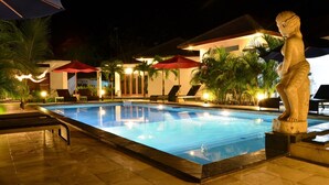 A nighttime swimming pool area with lounge chairs and umbrellas, surrounded by palm trees and a statue. - Explore Lombok From Your Villa for 2 or More (Senggigi)