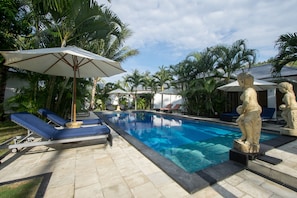 A swimming pool with lounge chairs and umbrellas, surrounded by palm trees and a clear sky.