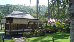 A wooden structure with a tiled roof, surrounded by a well-maintained garden with a lawn, stone pathway, and a small water feature. - Explore Lombok From Your Villa for 2 or More (Senggigi)