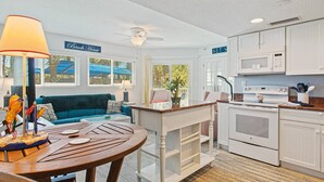Eine kompakte Küche mit weißen Schränken und einer Mikrowelle, ein Essbereich mit Holztisch und Stühlen sowie ein blaues Sofa im Wohnbereich.
