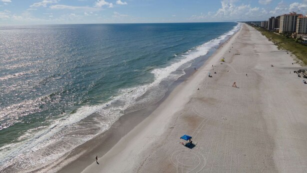 Ein Strand mit freiem Blick auf den Ozean, einem sandigen Ufer und einer Reihe von Gebäuden entlang der Küste.