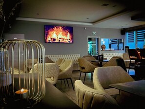 A modern lounge area with leather chairs, a table, and a fireplace mural on the wall. - City Vibes Hotel (Sindelfingen)