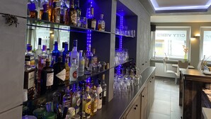 Un'area bar con scaffali pieni di bottiglie di liquori e bicchieri, un moderno design del soffitto e vista sulla città attraverso ampie finestre.