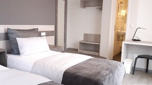 Camera d'albergo con due letti, una scrivania e un bagno visibile attraverso una porta aperta.