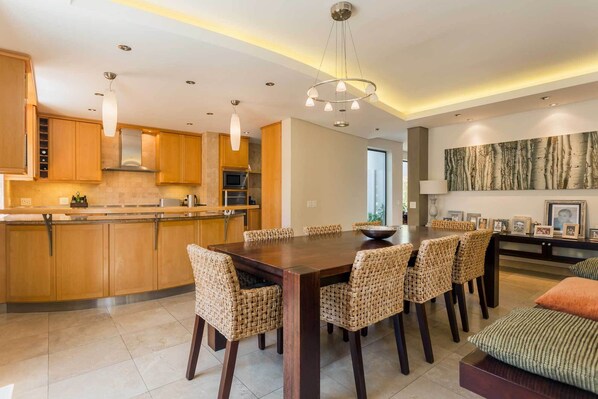 A modern kitchen with wooden cabinets, a dining area with wicker chairs, and a large dining table.