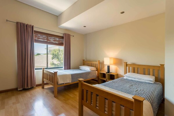 Une chambre à coucher avec deux lits en bois, une fenêtre avec des rideaux, une table de chevet avec une lampe et un luminaire au plafond.