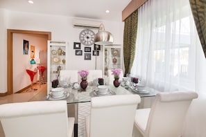 Een eetgedeelte met een glazen tafel, witte stoelen en een moderne hanglamp.