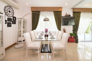 Een eetruimte met een glazen tafel, witte stoelen en een moderne kroonluchter.
