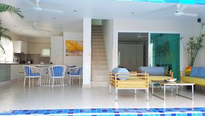 Ein modernes Wohnzimmer mit Esstisch, Stühlen, einer Couch und Blick auf den Pool.