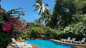 Ein Pool, umgeben von weißen Liegestühlen, Palmen und blühenden Büschen.