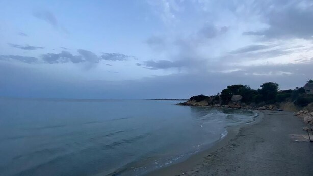 En strand med stilla vatten och en klippformation som syns på avstånd.