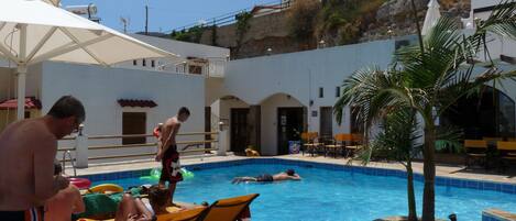 A swimming pool area with lounge chairs, a palm tree, and a building in the background.