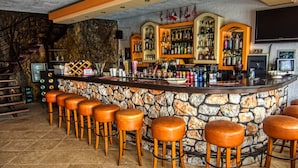 Een bar met een stenen toonbank, houten krukken en verschillende flessen en glazen.