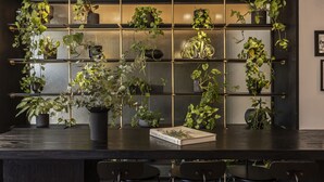 Un espace bar avec un comptoir en bois foncé, des chaises noires et une étagère à plantes fixée au mur.