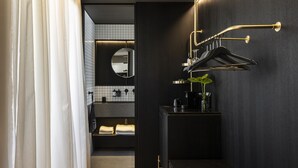 A modern bathroom with a dark wall, a black countertop, a round mirror, and a towel rack. - The Modernist Athens (Athens)