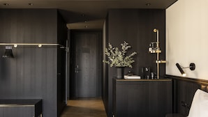 A modern hotel room with a dark wood finish, a bedside table with a lamp, a bed with a patterned bedspread, and a small plant on a nightstand. - The Modernist Athens (Athens)