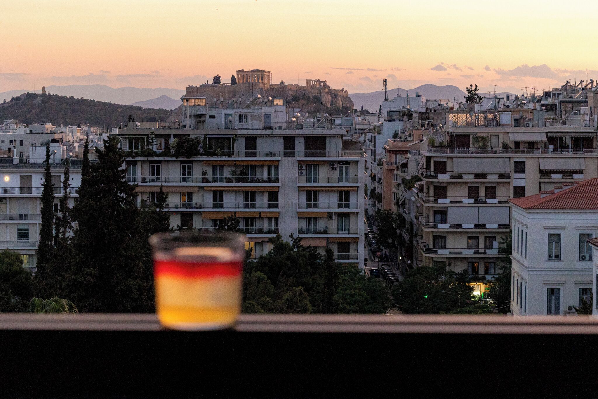 A cityscape with buildings, a distant mountain, and a glass with a red and yellow liquid.