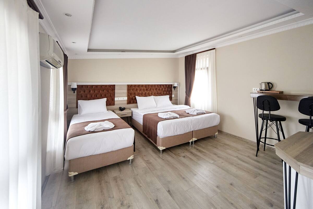 Habitación de hotel con dos camas, un escritorio con silla, cafetera y ventana con cortinas.