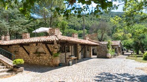 A stone building with a tiled roof, a cobblestone courtyard, and surrounding trees. - La Bastide du Riou (Bargemon)