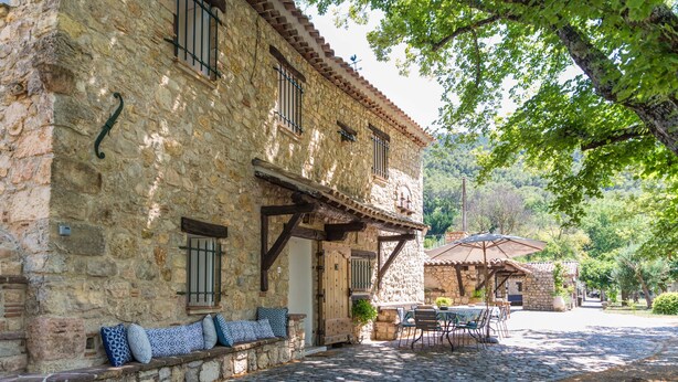 A stone building with a cobblestone patio, outdoor seating, and a small garden area. - La Bastide du Riou (Bargemon)