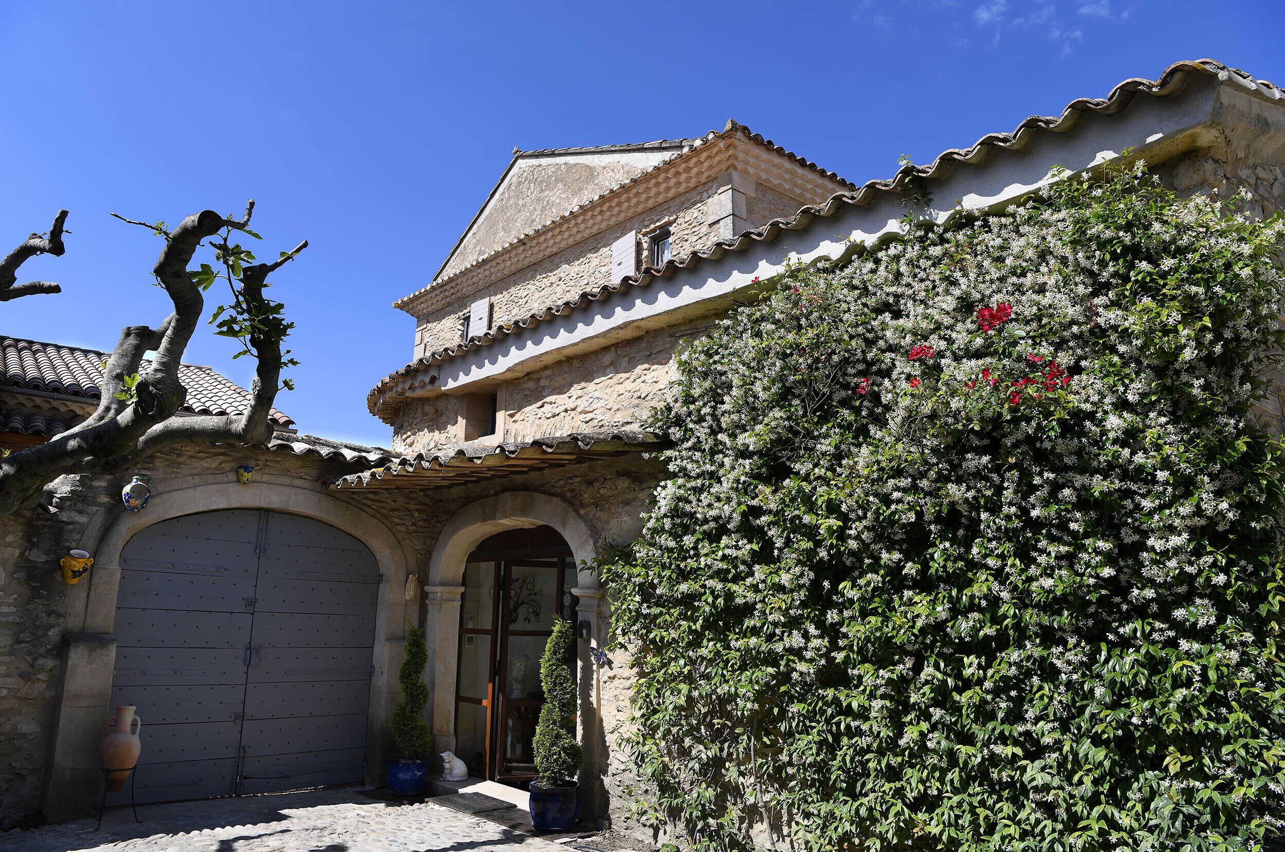 A traditional stone building with a tiled roof, a large arched entrance, and a potted plant in front.