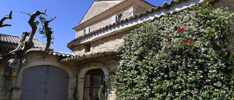 A traditional stone building with a tiled roof, a large arched entrance, and a potted plant in front.
