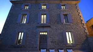A stone building with multiple windows and a door, featuring outdoor seating with white cushions. - Bastide Des Demoiselles (Roussillon)