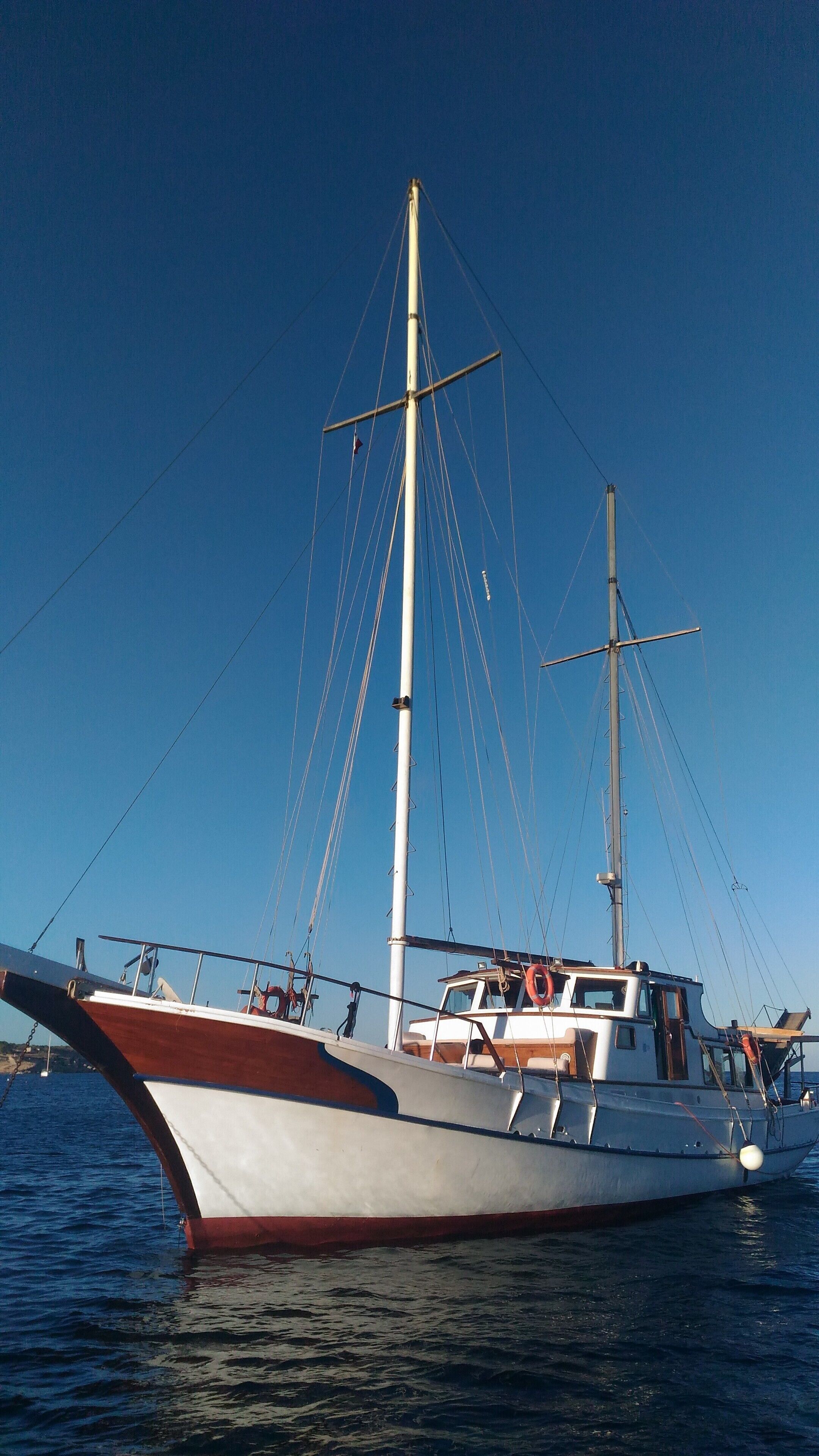 Un velero grande con un mástil alto y numerosas líneas de aparejo, anclado en aguas tranquilas.