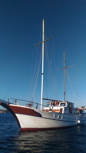 A large sailing boat with a tall mast and multiple rigging lines, anchored in calm waters.