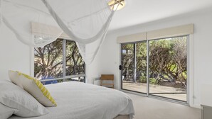Een slaapkamer met een groot bed, een plafondventilator en uitzicht op een terras en bomen door een schuifdeur.