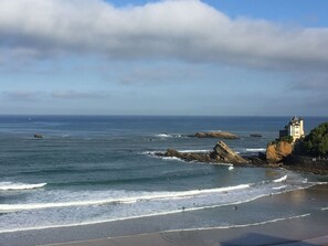 A coastal scene with a castle on a cliff overlooking the sea, waves crashing onto the shore, and a clear sky.