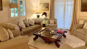 Een gezellige woonkamer met een houten plafond, een bank, een fauteuil, een salontafel en een lamp.