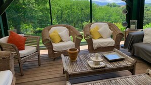 Een overdekt terras met rieten stoelen, een houten tafel en uitzicht op weelderige begroeiing.