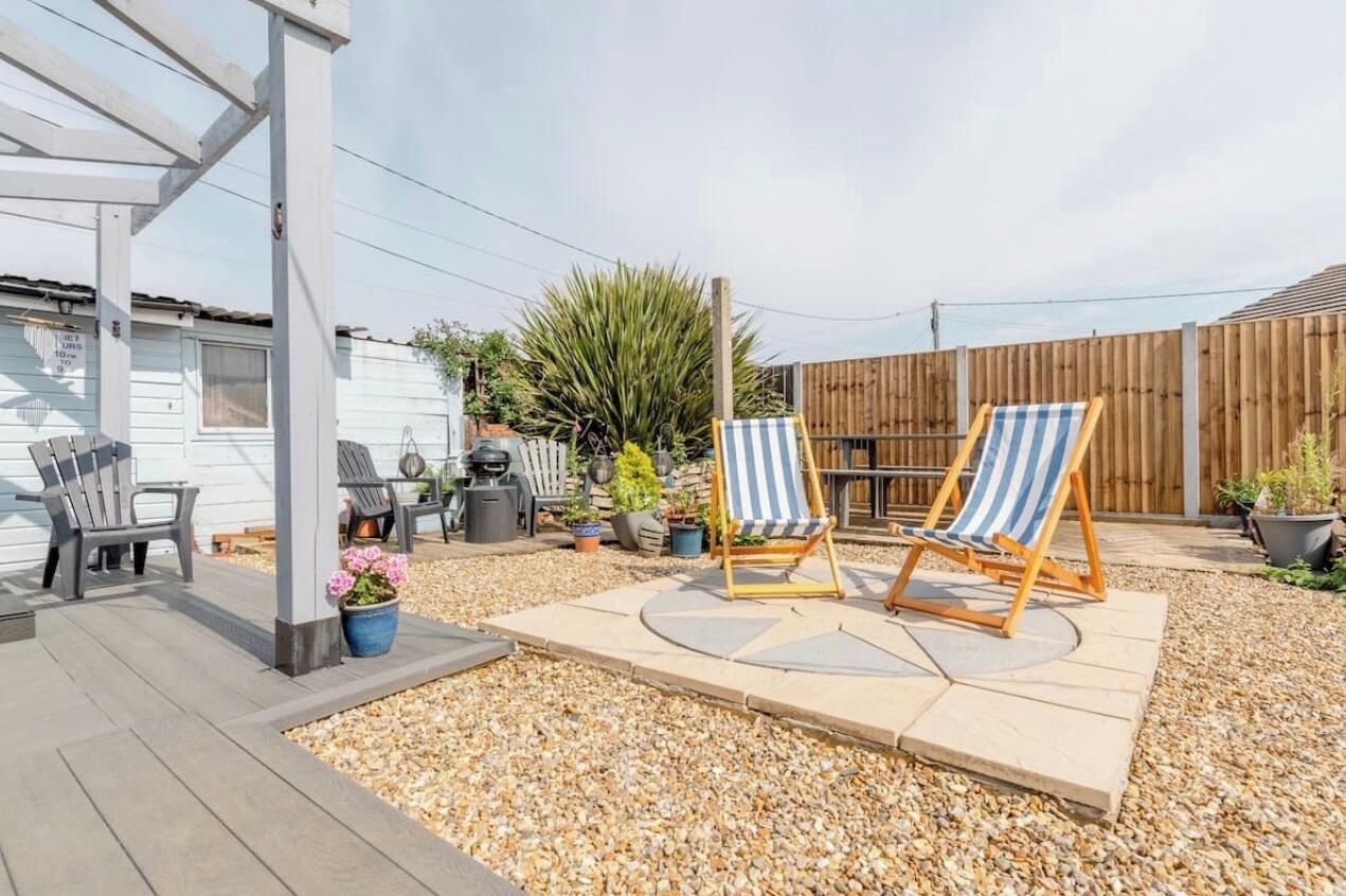 Un jardin avec une terrasse en bois, deux chaises longues à rayures, un barbecue et une clôture en bois.