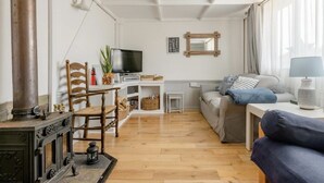 A cozy living room with a wooden floor, a sofa, a TV, a fireplace, and a window with curtains.