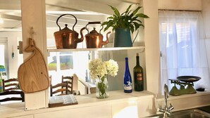 A kitchen with a wooden cutting board, copper teapots, a potted plant, a vase with flowers, and wine bottles.