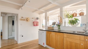 A modern kitchen with wooden cabinets, a dishwasher, and a window with plants.