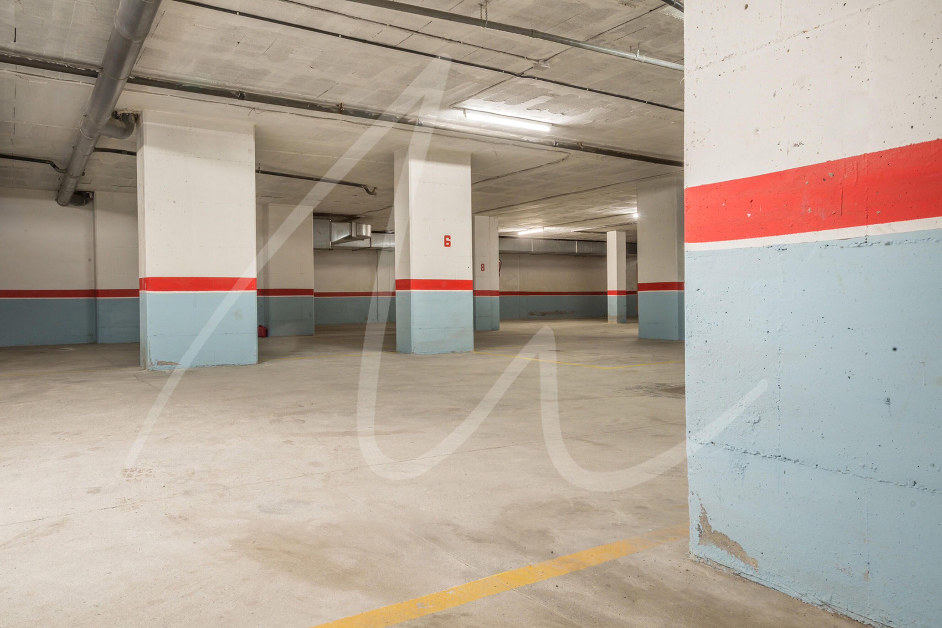 Un parking intérieur avec des piliers en béton, des lignes jaunes délimitant les places et des murs peints en rouge et en bleu.