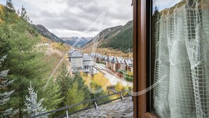 A view from a window overlooking a valley with buildings, trees, and mountains. - Sarrahèra (Baqueira)