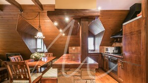 A wooden interior with a stone island, wooden dining table, chairs, and a kitchen area with appliances. - Sarrahèra (Baqueira)