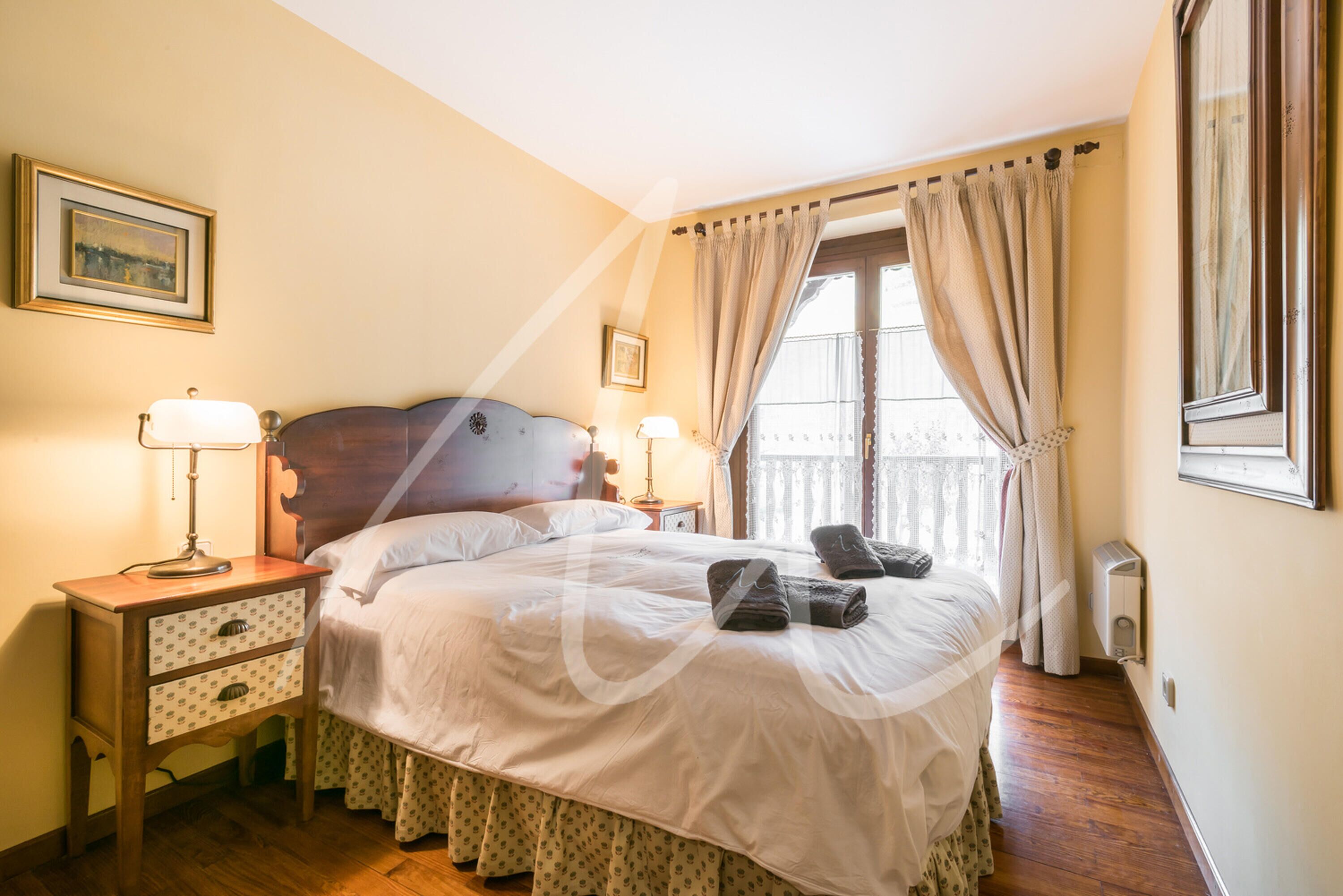 Un lit bien fait, avec une tête de lit en bois, deux tables de chevet avec des lampes et une fenêtre avec des rideaux.