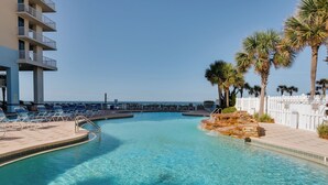 En klarblå pool med ett vattenfall av sten som dekorativt inslag, omgiven av solstolar och palmer.