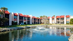 Un hôtel avec un bâtiment à toit rouge, un petit étang agrémenté d’une fontaine et une pelouse bien entretenue.